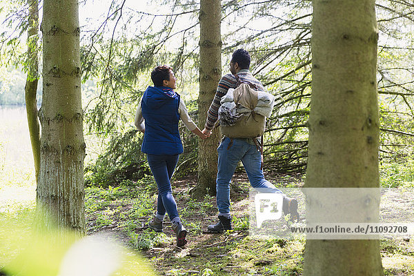 Paar beim Händchenhalten und Wandern mit Rucksack im Wald