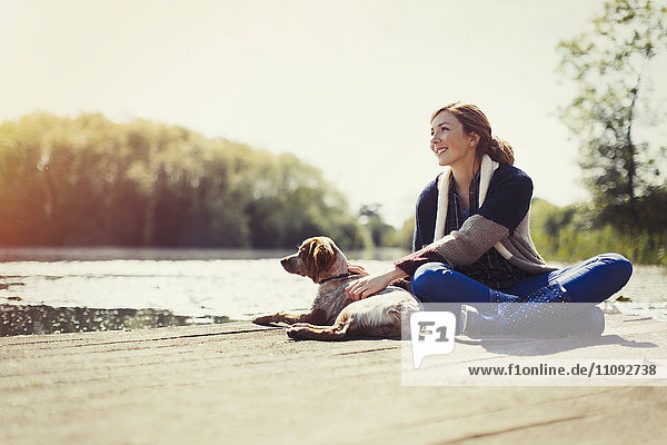 Smiling woman and dog relaxing on sunny lakeside dock
