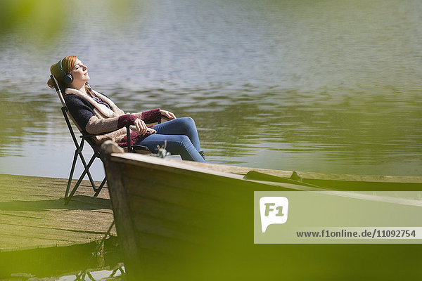 Serene woman relaxing listening to music with headphones at sunny lakeside dock