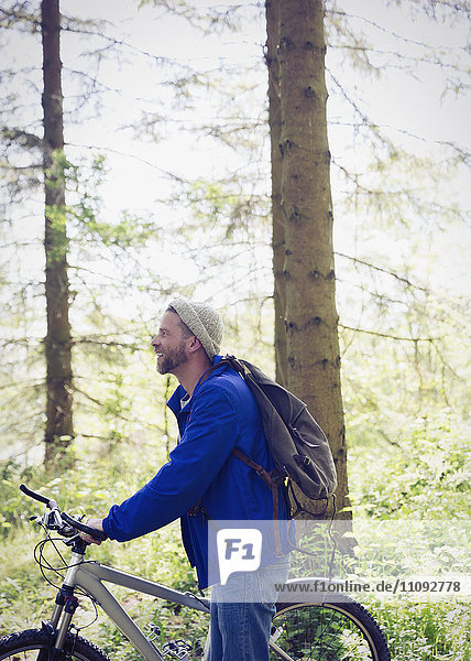 Mann mit Rucksack und Mountainbike im sonnigen Wald