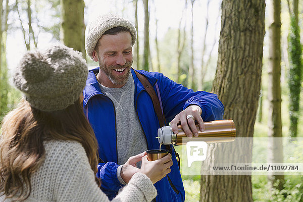 Couple hiking and drinking coffee from insulated drink container in woods