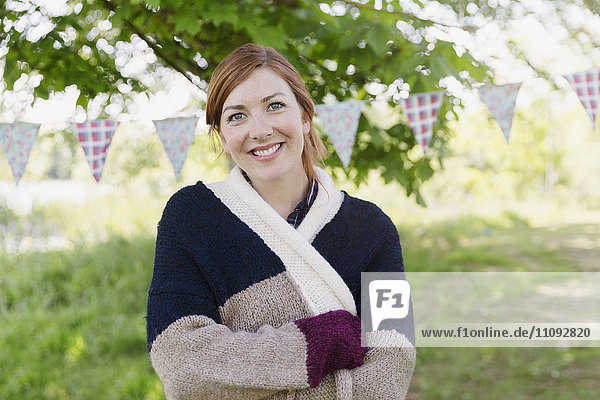 Portrait smiling woman in warm sweater in front of party banner in backyard