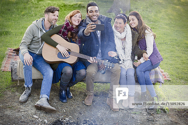 Freunde mit Gitarre nehmen Selfie mit Fotohandy auf dem Campingplatz mit.