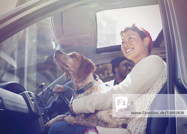 Lächelnde Frau hält Hund auf Schoß im Auto