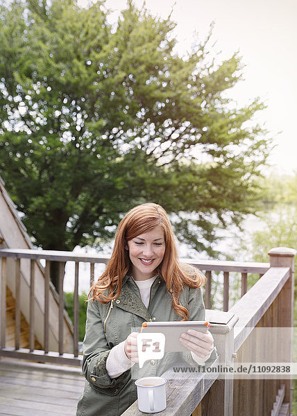 Smiling woman with red hair using digital tablet on cabin balcony