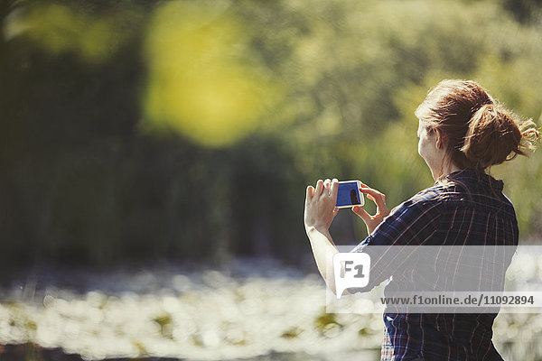 Woman using camera phone at sunny lakeside
