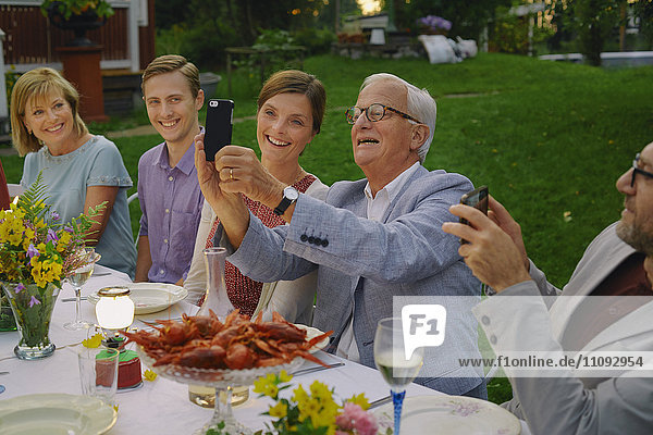 Senior Mann nimmt Selfie mit Familie beim Sommergartenparty-Dinner mit