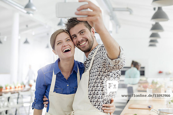 Enthusiastic couple taking selfie with camera phone in cooking class kitchen
