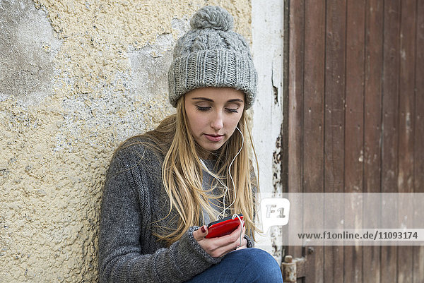 Teenager-Mädchen hört Musik auf dem Mobiltelefon und lehnt sich an die Wand