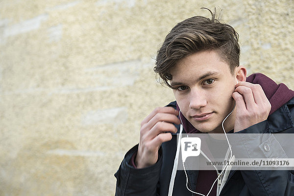 Porträt eines jungen Mannes  der mit Ohrstöpseln Musik hört
