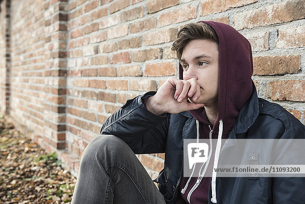 Young man sitting against brick wall and thinking