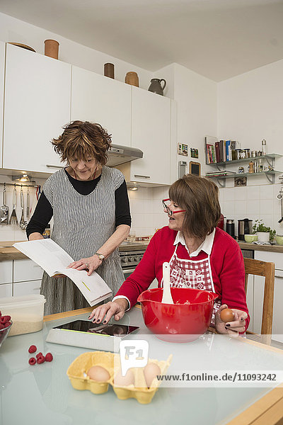 Two senior woman comparing recipe on digital tablet and cookery book