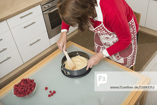 Senior woman filling dough into a spring form pan and making smooth