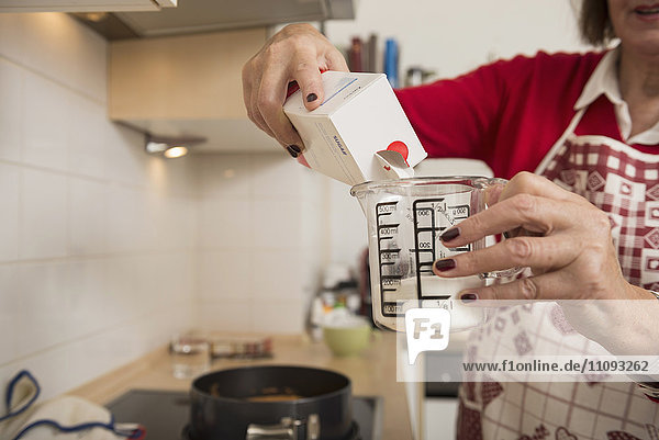 Senior woman filling icing sugar into a measuring cup in kitchen