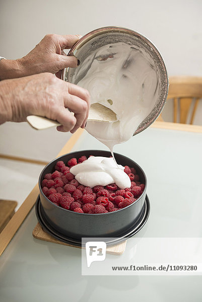 Senior woman pouring meringue on cake base and berries in springform pan