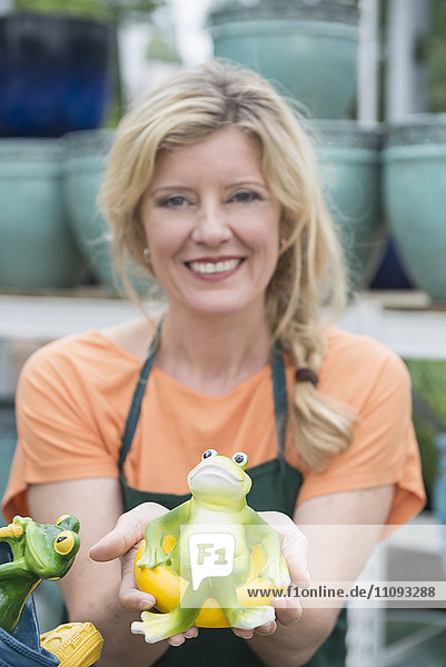 Female shop assistant showing artificial frog in garden centre Augsburg Bavaria Germany