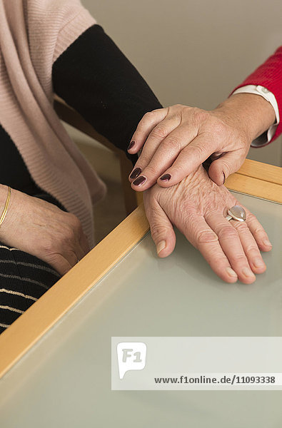 Die Hände zweier älterer Frauen trösten sich gegenseitig