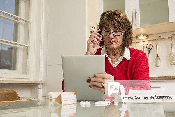 Ältere Frau liest Beipackzettel für Tabletten auf digitalem Tablet