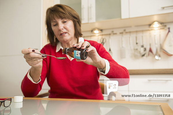 Senior woman pouring liquid medicine in a spoon in the kitchen