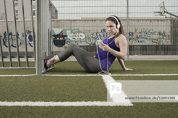 Junge Frau  die sich nach dem Training ausruht und auf dem Fußballplatz Musik hört
