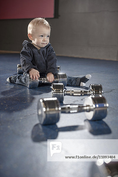 Nettes kleines Baby spielt mit Hanteln im Fitnessstudio
