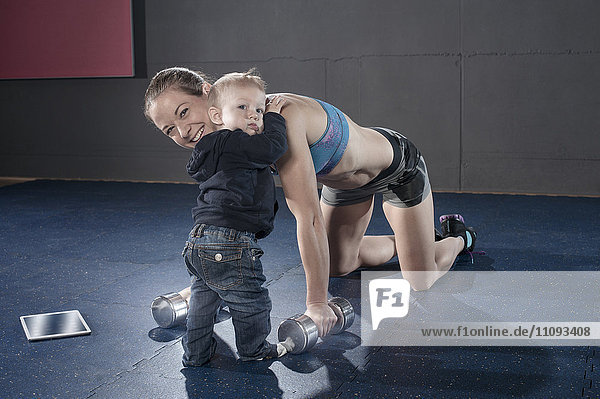 Kleiner Junge umarmt seine Mutter in der Turnhalle  während seine Mutter Übungen macht