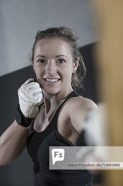 Junge Frau macht Krafttraining  indem sie auf einen Boxsack im Fitnessstudio schlägt