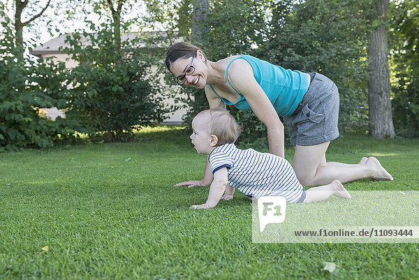 Baby son with his mother crawling in lawn  Munich  Bavaria  Germany