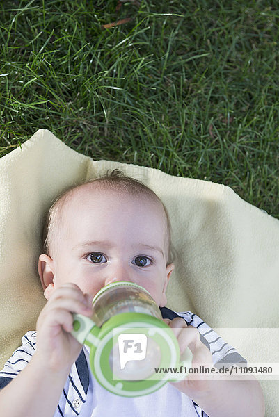 Baby boy drinking from a baby bottle lying in lawn  Munich  Bavaria  Germany