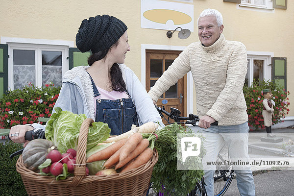 Ehepaar mit Fahrrädern und Gemüse auf der Straße vor einem Bioladen
