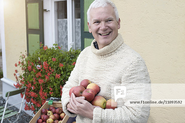 Älterer Mann mit Äpfeln in der Hand vor einem Naturkostladen und lächelnd