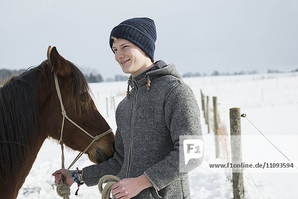 Young man with horse standing in snowy landscape  Bavaria  Germany