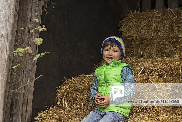 Kleiner Junge sitzt auf Stroh im Stall und lächelt
