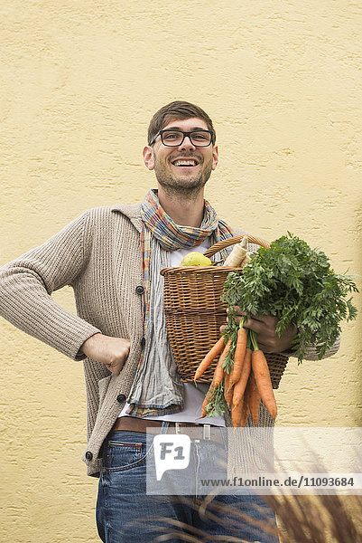 Porträt eines erwachsenen Mannes  der einen Korb voller Gemüse hält und lächelt