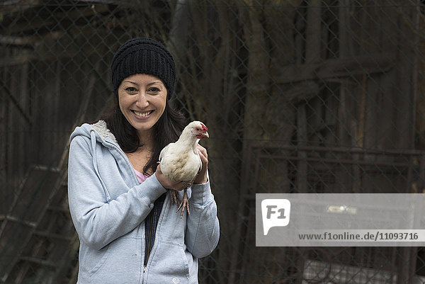 Porträt einer Bäuerin mit weißem Huhn und lächelndem Vogel auf dem Bauernhof