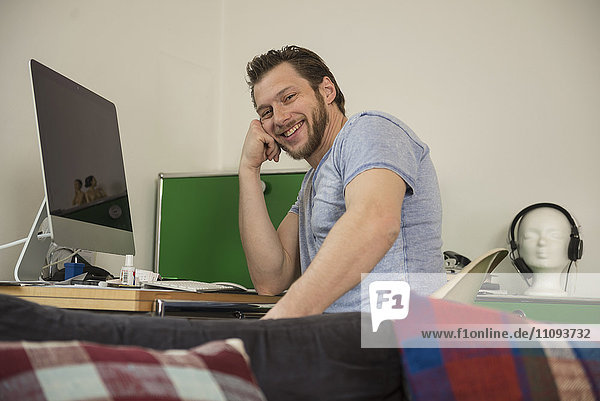 Mid adult man working on computer in living room and smiling  Munich  Bavaria  Germany