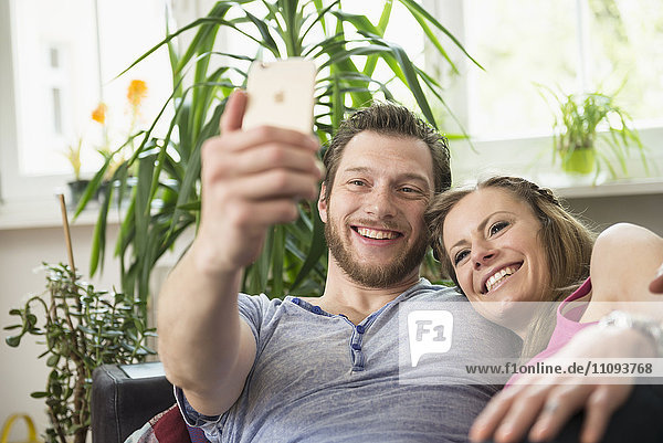 Couple taking selfie in living room and smiling  Munich  Bavaria  Germany