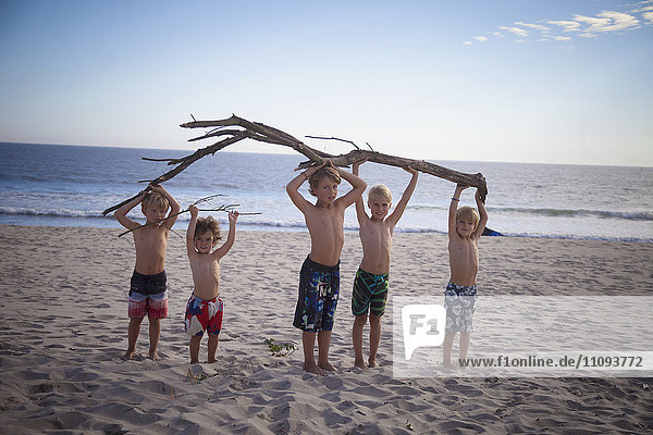 Eine Gruppe von Kindern hält einen Baumstamm am Strand hoch