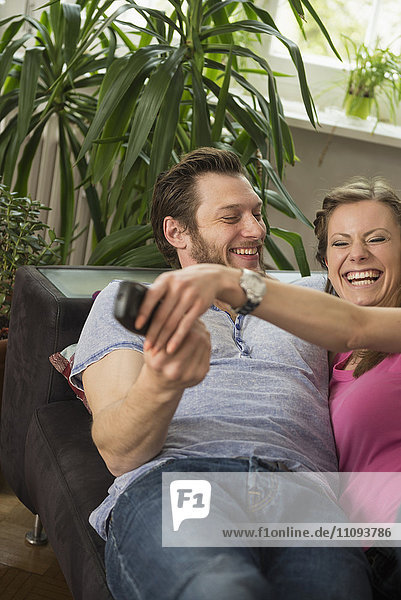 Couple fighting for remote in living room  Munich  Bavaria  Germany