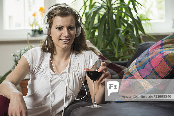 Porträt einer jungen Frau beim Musikhören und Weintrinken im Wohnzimmer  München  Bayern  Deutschland