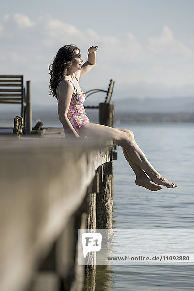 Mature woman sitting in swimsuit on pier and looking at distance  Bavaria  Germany