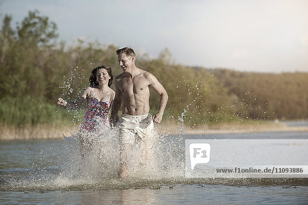 Mature couple running through the water in lake  Bavaria  Germany