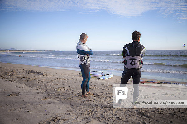 Zwei Surfer schauen auf das Meer und stehen am Strand