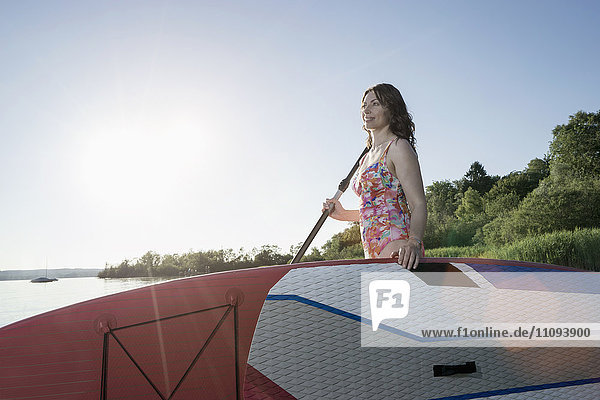 Mature woman carrying stand up paddle board at lakeshore  Bavaria  Germany