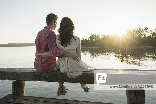 Mature couple sitting on pier looking at sunset  Bavaria  Germany