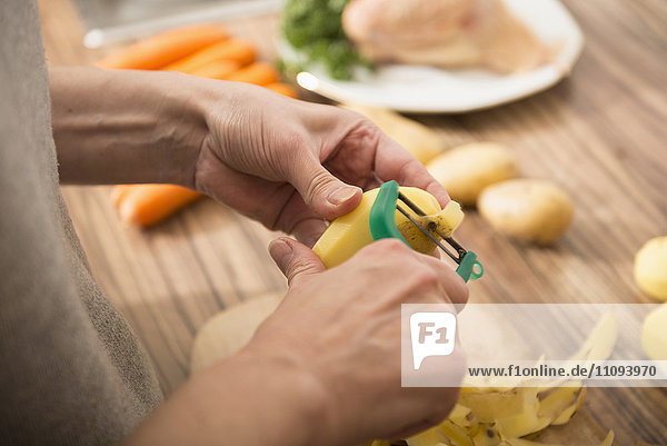 Frau schält Kartoffeln mit einem Kartoffelschäler in der Küche