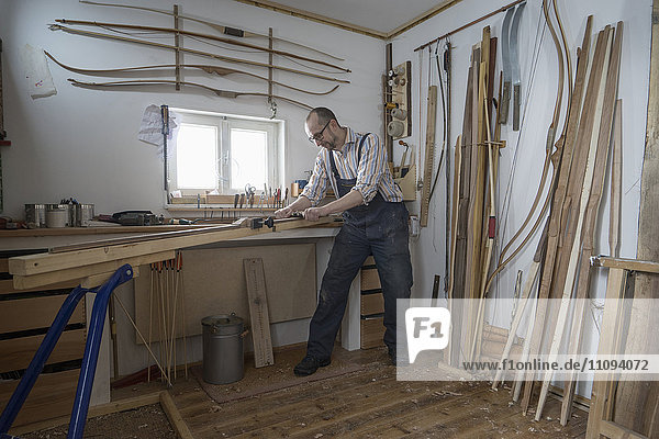 Männlicher Bogenbauer,  der Holz spaltet und es in Form eines Bogens bringt,  in einer Werkstatt,  Bayern,  Deutschland