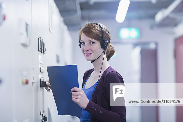 Porträt einer jungen Ingenieurin  die ein Headset trägt und eine Schaltanlage im Kontrollraum steuert