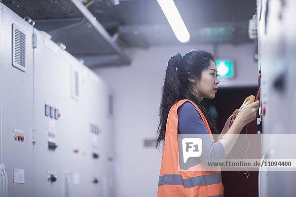 Junge Ingenieurin  die eine Steuertafel mit einem Multimeter in einer Industrieanlage untersucht
