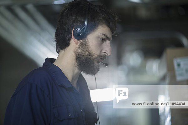 Junger männlicher Ingenieur  der ein Headset trägt und in einer Industrieanlage arbeitet